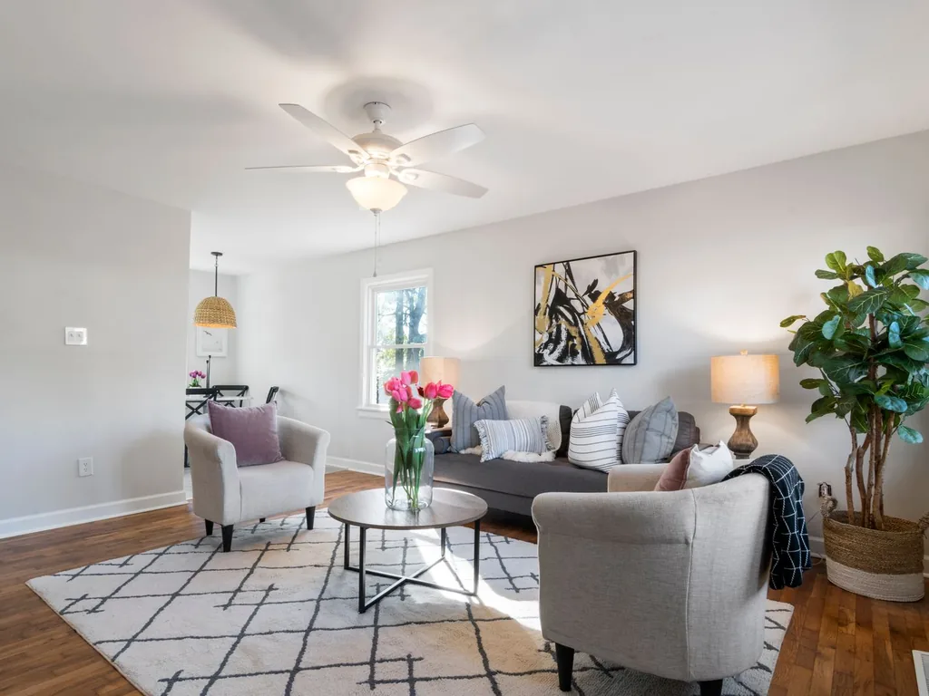Bright, plainly furnished living room before AI room redesign — charcoal sofa, black-and-white geometric rug, ceiling fan and window in place